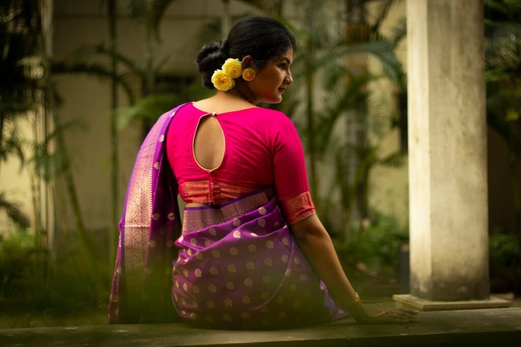 pexels photo 19282458 A back view of an Indian woman in traditional attire sitting outdoors, adorned with yellow flowers.