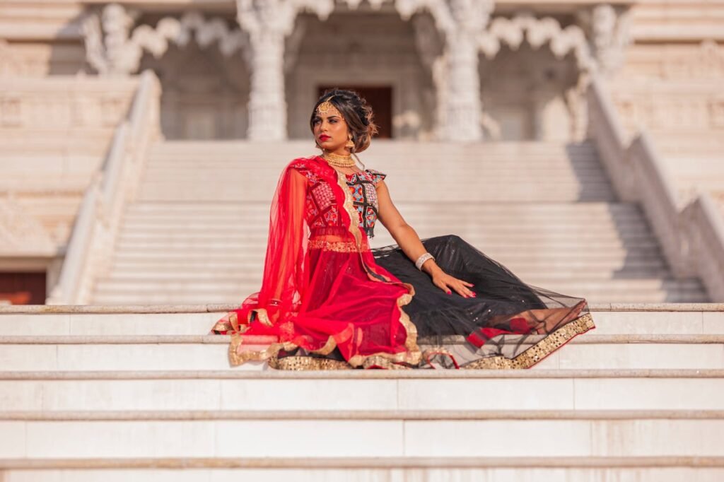 pexels photo 34222609 2 Stylish Indian woman in vibrant red and black traditional dress sitting gracefully on temple steps in Atlanta, GA.